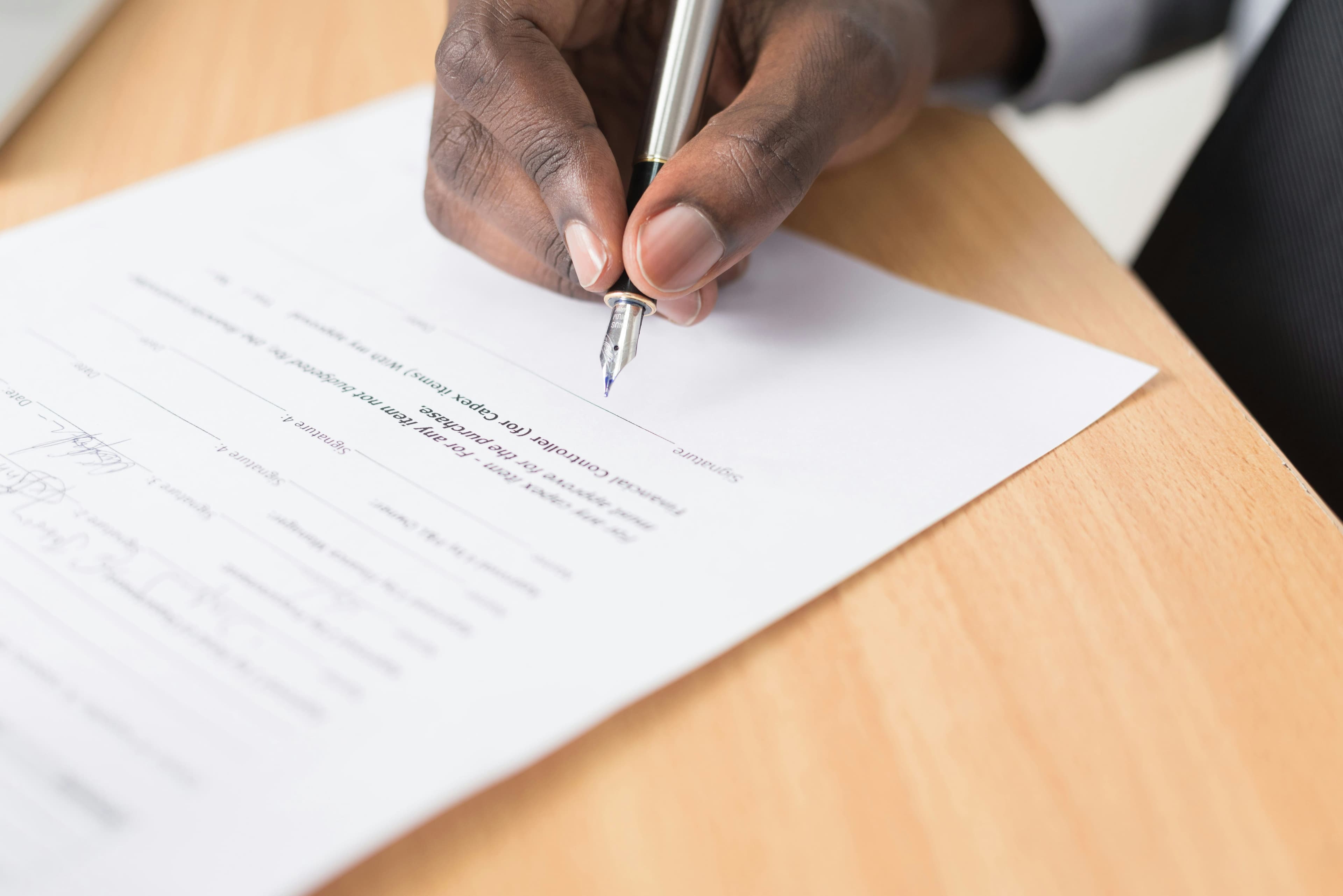 Signing and managing contractor agreements Close up of a person signing a contract document with a pen on a wooden desk