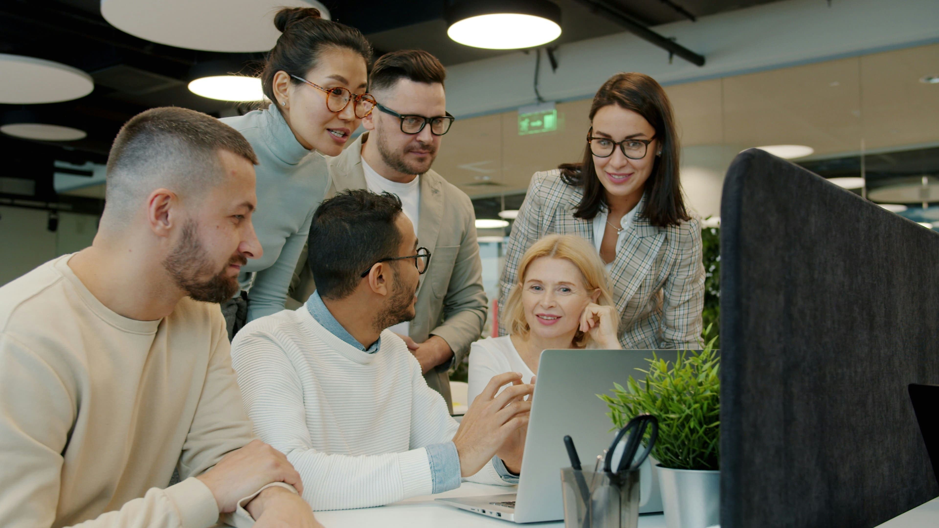 Your new hire integrates with your team quickly Team gathered around a laptop in a modern office collaborating with a new member during onboarding